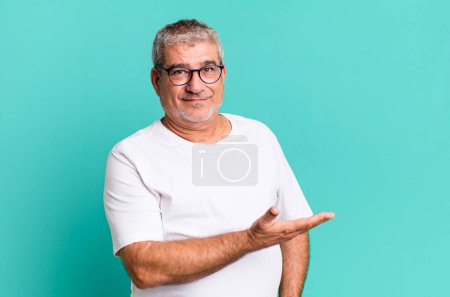 Foto de Hombre mayor de mediana edad sonriendo alegremente, sintiéndose feliz y mostrando un concepto en espacio de copia con palma de la mano - Imagen libre de derechos