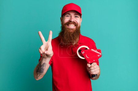 Photo for Long beard man smiling and looking happy, gesturing victory or peace. shipping packer concept - Royalty Free Image
