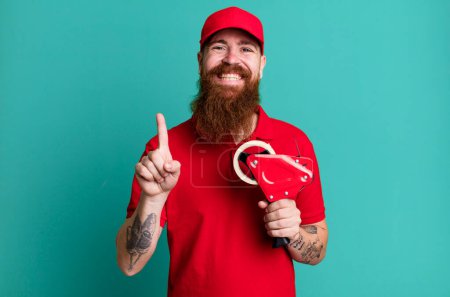 Téléchargez les photos : Barbe longue homme souriant et l'air amical, montrant numéro un. concept d'emballeur d'expédition - en image libre de droit
