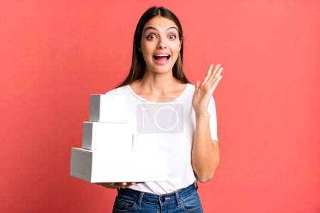 Foto de Joven bonita mujer sintiéndose feliz y asombrada por algo increíble. cajas blancas en blanco - Imagen libre de derechos