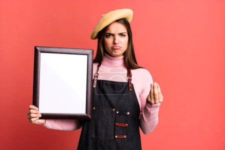 Photo for Young pretty woman making capice or money gesture, telling you to pay. empty picture frame concept - Royalty Free Image