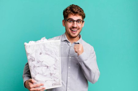 Téléchargez les photos : Jeune homme caucasien adulte se sentant heureux et faisant face à un défi ou célébrer avec un concept de poubelle de boules de papier - en image libre de droit