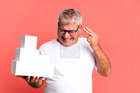 Photo for Middle age senior man looking unhappy and stressed, suicide gesture making gun sign. different packages blank boxes - Royalty Free Image