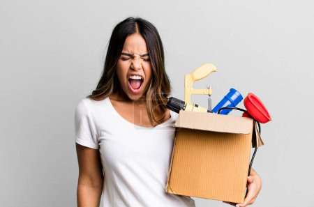 Photo for Hispanic pretty woman shouting aggressively, looking very angry. housekeeper with a toolbox concept - Royalty Free Image