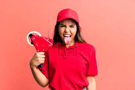 Photo for Hispanic pretty woman with cheerful and rebellious attitude, joking and sticking tongue out. packer and delivery employee - Royalty Free Image