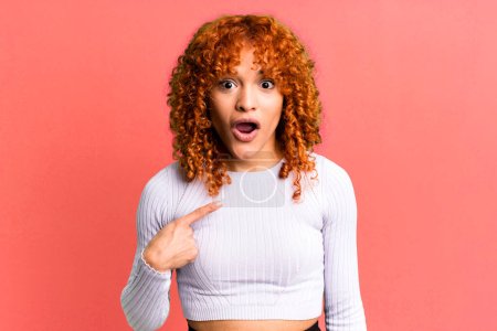 Photo for Redhair pretty woman looking shocked and surprised with mouth wide open, pointing to self - Royalty Free Image