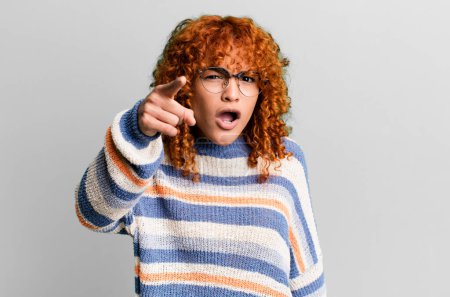 Foto de Redhair pretty woman pointing at camera with an angry aggressive expression looking like a furious, crazy boss - Imagen libre de derechos