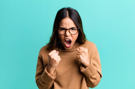 Photo for Hispanic pretty woman shouting aggressively with annoyed, frustrated, angry look and tight fists, feeling furious - Royalty Free Image
