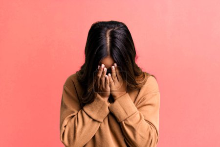 Foto de Mujer bonita hispana sintiéndose triste, frustrada, nerviosa y deprimida, cubriendo la cara con ambas manos, llorando - Imagen libre de derechos