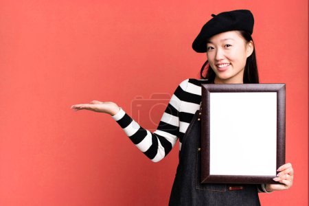 Foto de Young adult pretty asian woman with a beret and an empty picture frame - Imagen libre de derechos