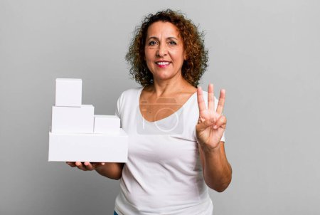 Photo for Pretty middle age woman smiling and looking friendly, showing number three. blank white boxes packaging - Royalty Free Image