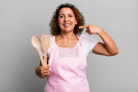 Photo for Pretty middle age woman smiling confidently pointing to own broad smile. home wife chef concept - Royalty Free Image