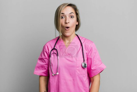 Photo for Pretty blonde woman looking very shocked or surprised. nurse concept - Royalty Free Image