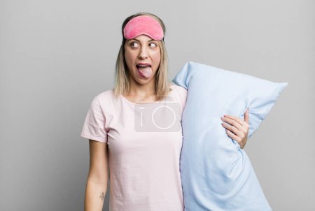 Foto de Bonita mujer rubia con actitud alegre y rebelde, bromeando y sacando la lengua. concepto de pijamas y ropa de dormir - Imagen libre de derechos