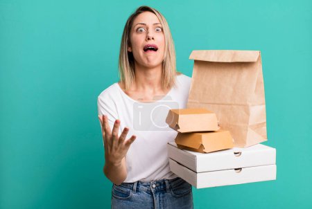 Photo for Pretty blonde woman looking desperate, frustrated and stressed. paper fast food take away packages - Royalty Free Image