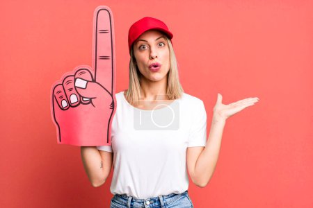 Photo for Pretty blonde woman looking surprised and shocked, with jaw dropped holding an object. number one fan concept - Royalty Free Image