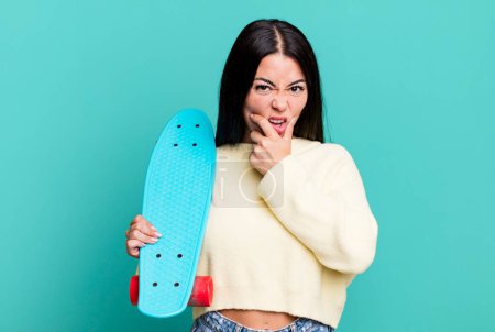 Photo for Hispanic pretty woman with mouth and eyes wide open and hand on chin. skate boarding concept - Royalty Free Image