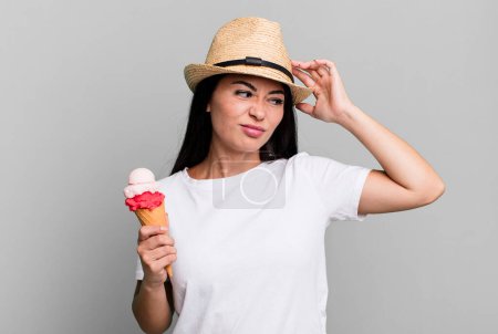 Téléchargez les photos : Jolie femme hispanique souriant joyeusement et rêvant ou doutant. crème glacée et concept d'été - en image libre de droit