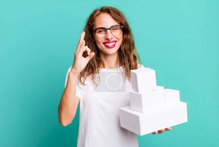 Photo for Hispanic pretty woman feeling happy, showing approval with okay gesture. with white boxes packages - Royalty Free Image