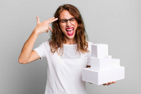 Photo for Hispanic pretty woman looking unhappy and stressed, suicide gesture making gun sign. with white boxes packages - Royalty Free Image
