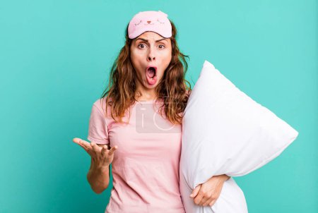 Photo for Hispanic pretty woman amazed, shocked and astonished with an unbelievable surprise wearing pajamas and a pillow - Royalty Free Image
