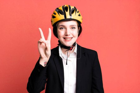 Foto de Joven mujer bonita sonriendo y mirando feliz, haciendo gestos de victoria o paz. concepto de bicicleta y mujer de negocios - Imagen libre de derechos