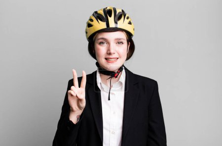 Téléchargez les photos : Jeune jolie femme souriante et sympathique, montrant le numéro deux. concept vélo et femme d'affaires - en image libre de droit