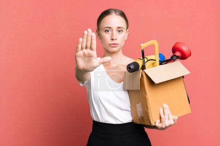 Photo for Caucasian pretty woman looking serious showing open palm making stop gesture with a tool box. repair home concept - Royalty Free Image