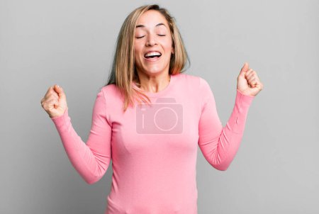Foto de Mujer adulta rubia mirando extremadamente feliz y sorprendida, celebrando el éxito, gritando y saltando - Imagen libre de derechos