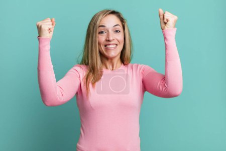 Foto de Blonde adult woman celebrating an unbelievable success like a winner, looking excited and happy saying take that! - Imagen libre de derechos