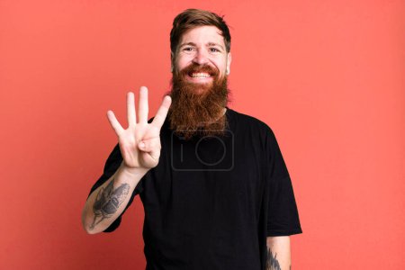 Téléchargez les photos : Barbe longue et cheveux roux homme souriant et regardant amical, montrant numéro quatre - en image libre de droit