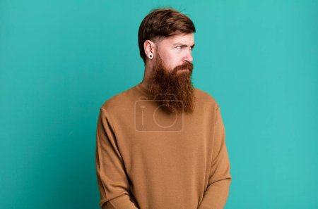 Téléchargez les photos : Barbe longue et cheveux roux homme se sentant triste, contrarié ou en colère et regardant vers le côté - en image libre de droit