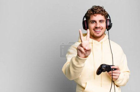 Photo for Young adult caucasian man smiling and looking friendly, showing number two with headset and a controller. gamer concept - Royalty Free Image