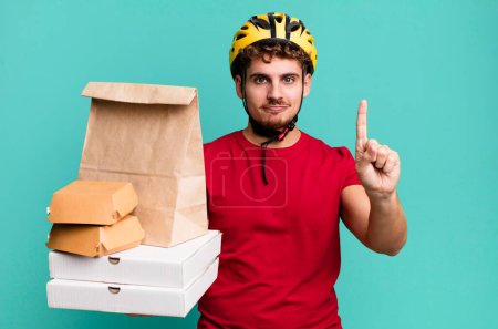 Foto de Joven adulto caucásico hombre sonriendo y buscando amigable, mostrando el número uno. llevar concepto de entrega de comida rápida - Imagen libre de derechos