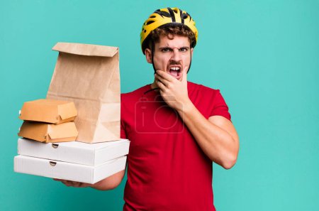 Photo for Young adult caucasian man with mouth and eyes wide open and hand on chin.  take away fast food deliveryman concept - Royalty Free Image