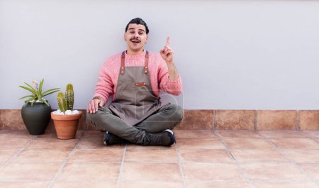 Photo for Young handsome man gardering and sitting on the floor outdoors - Royalty Free Image