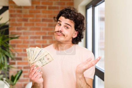 Téléchargez les photos : Jeune homme beau avec des billets en dollars à l'intérieur de la maison - en image libre de droit