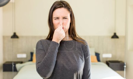 Photo for Young adult pretty woman feeling disgusted, holding nose to avoid smelling a foul and unpleasant stench - Royalty Free Image