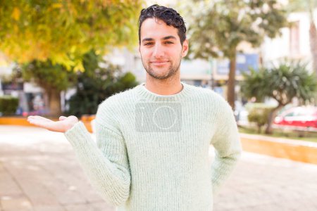 Téléchargez les photos : Jeune homme hispanique souriant, se sentant confiant, réussi et heureux, montrant concept ou idée sur l'espace de copie sur le côté - en image libre de droit