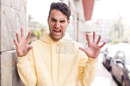 Photo for Young hispanic man screaming in panic or anger, shocked, terrified or furious, with hands next to head - Royalty Free Image