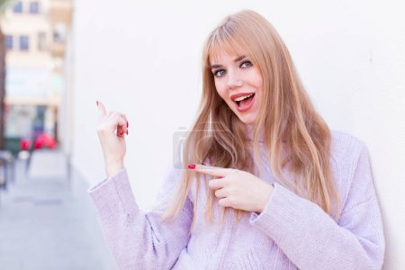 Photo for Young pretty woman feeling joyful and surprised, smiling with a shocked expression and pointing to the side - Royalty Free Image