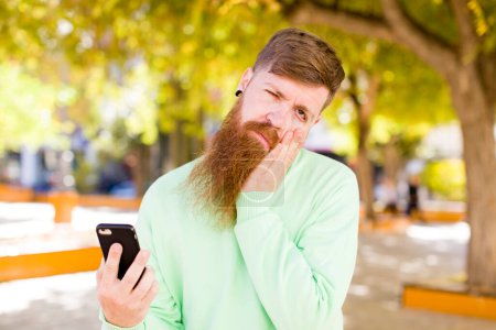 Téléchargez les photos : Jeune homme barbu adulte se sentant ennuyé, frustré et somnolent après un fatigant avec un smartphone - en image libre de droit