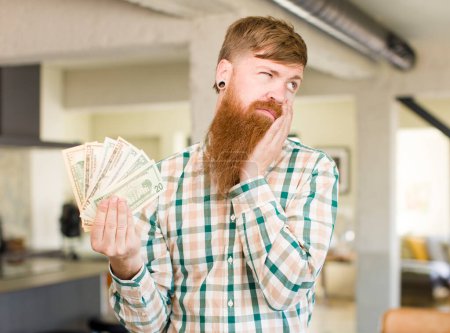 Photo for Red hair man feeling bored, frustrated and sleepy after a tiresome with dollar banknotes - Royalty Free Image