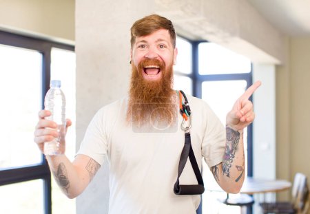 Photo for Red hair man smiling cheerfully, feeling happy and pointing to the side with a water bottle. fitness concept - Royalty Free Image