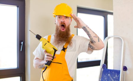 Téléchargez les photos : Homme aux cheveux roux regardant heureux, étonné et surpris réparer la maison. concept bricoleur - en image libre de droit