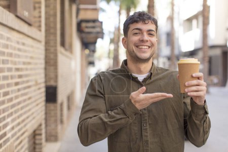 Photo for Young handsome man smiling cheerfully, feeling happy and showing a concept. take away coffee concept - Royalty Free Image