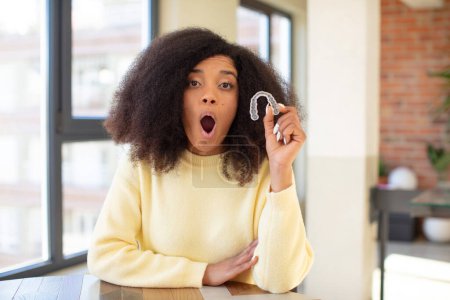 Téléchargez les photos : Jolie afro femme noire se sentant extrêmement choqué et surpris. concept de retenue dentaire - en image libre de droit