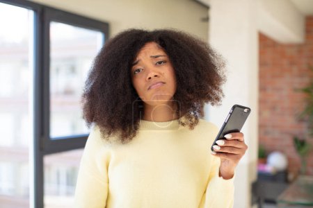 Photo for Pretty afro black woman feeling sad and whiney with an unhappy look and crying. smartphone concept - Royalty Free Image