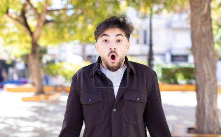 Photo for Young handsome man looking very shocked or surprised, staring with open mouth saying wow - Royalty Free Image