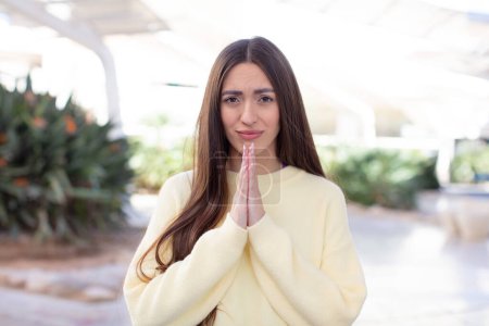 Photo for Young pretty woman feeling worried, hopeful and religious, praying faithfully with palms pressed, begging forgiveness - Royalty Free Image